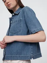 Camisa de jean de corte recto y largo a la cintura, con cuello clásico, cierre frontal de botones y un bolsillo aplicado en el pecho.