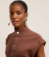 Mono largo de sarga color marrón, con cuello alto, cierre frontal con botones ocultos, sin mangas y bolsillos laterales. Incluye trabillas para cinturón.