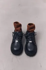 Zapatos de cuero negro con cordones, diseño robusto y suela track dentada. Presentan un detalle metálico en el centro de los cordones.