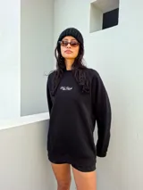 Buzo oversize de algodón color negro, con cuello redondo, mangas largas y estampa frontal pequeña con texto bordado.