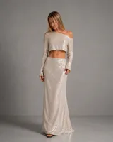 Conjunto de dos piezas en color champagne, bordado íntegramente con lentejuelas. Incluye un top de manga larga con escote asimétrico de hombros descubiertos y una falda larga de corte recto y caída fluida.