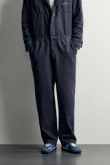 Mono oversize fit de algodón con estructura espiga en color azul marino, con cuello solapa en contraste de color tostado, manga larga, bolsillos de plastrón en el pecho con firma bordada, trabillas laterales en la cintura y cierre frontal con cremallera y botonadura oculta.