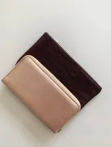Billetera rectangular de gran tamaño en color rosa metalizado, con cierre perimetral y tirador metálico dorado.