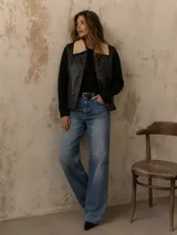 Chaleco de cuero negro con cuello de corderito sintético, cierre frontal y diseño de paneles con costuras visibles.