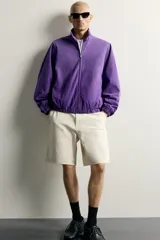 Cazadora relaxed fit de denim de algodón en color violeta, con efecto lavado, cuello alto, cierre frontal de cremallera y bolsillos en las costuras laterales. Presenta puños y dobladillo elásticos.