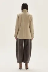 Blazer de paño color beige, con solapas clásicas y bordados decorativos en tono más oscuro en la parte inferior de las mangas.