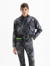 Chaqueta estilo bomber confeccionada en gabardina con estampado de damasco. Presenta cierre frontal oculto por carterón, bolsillos con tapa en forma de V y detalles tejidos en cuello y ruedo.