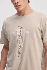 Remera de algodón color beige con efecto desgastado, cuello redondo, manga corta y estampa frontal con tipografía en tonos marrón y blanco.