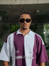 Chomba de piqué con diseño color block vertical en negro y verde oscuro, cuello polo y cierre frontal parcial. Presenta inscripciones en el frente.