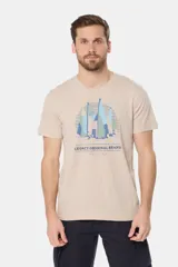 Remera de manga corta color verde grisáceo con cuello redondo. Presenta un estampado frontal de veleros sobre un fondo circular con líneas verticales, y texto bordado debajo.