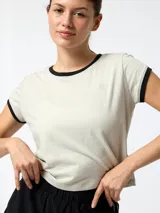 Remera de manga corta estilo crop, color gris claro con detalles en negro en el cuello y en los bordes de las mangas. Presenta un pequeño logo bordado en el pecho.