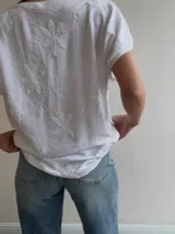 Blusa blanca de corte relajado, con escote en V, mangas cortas amplias y detalles de bordados florales en relieve.