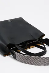 Bolso de hombro tipo tote bag de piel vacuna color beige, con doble asa de mano y correa ajustable de tejido. Presenta un cierre de cordón en la parte superior y un logo metálico en relieve en el frente. Incluye bolsillo interior con cierre de cremallera.