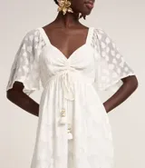 Vestido largo evasé de crepé blanco con textura y volados. Tiene escote corazón, elástico en la cintura, lazo con cordón y borla en las puntas, y mangas cortas.