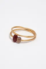 Pulsera rígida de aleación dorada con acabado mate, compuesta por dos aros entrelazados y decorada con dos cuentas de piedra en tonos marrón y gris.