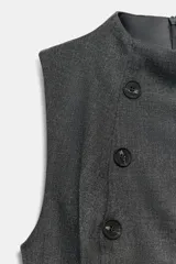 Top sin mangas de cuello subido, con diseño estructurado y cierre frontal de doble botonadura. Presenta trabillas decorativas en los laterales y forro interior.