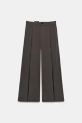 Pantalón de tiro medio con corte wide leg, presenta pliegues frontales, bolsillos laterales y trabilla con botón en la espalda. Cierre frontal con cremallera y botón.