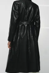 Trench de corte largo confeccionado en piel 100% con acabado brillante. Presenta cuello alto, hombreras marcadas, manga larga, bolsillos con solapa en el delantero y cierre frontal con botones. Incluye un cinturón ajustable del mismo material para entallar la silueta.