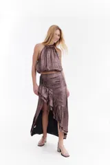 Falda midi color marrón metalizado, con tajo frontal, detalles de tablas en la cintura y volados diagonales.