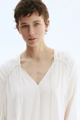Blusa oversized de viscosa color beige con escote en V pronunciado, cordones ajustables con cuentas en los extremos, hombros caídos y mangas globo largas con puños elásticos.