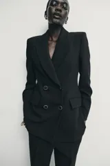 Blazer de corte estructurado con hombreras, cuello solapa y manga larga. Presenta un diseño cruzado con cierre frontal de botones y bolsillos delanteros con solapa.