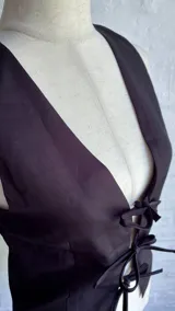 Chaleco negro con escote en V profundo y cierre frontal mediante lazos ajustables.