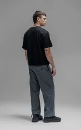Pantalón de corte oversize color gris carbón, confeccionado en microfibra técnica. Presenta cintura elástica, bolsillos laterales, un bolsillo cargo con cierre de broche y sistema de elásticos con tancas en los tobillos para regular la apertura.