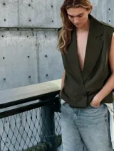 Chaleco de cuello solapa y escote pico cruzado, con hombreras y manga sisa. Presenta bolsillos de vivo en el delantero, forro interior y cierre frontal cruzado con botones. Incluye un cinturón de lazada en el mismo tejido.