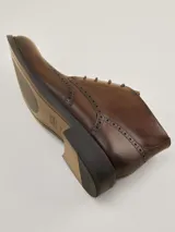 Botas de cuero marrón oscuro estilo brogue, con cordones y suela baja.