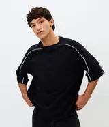 Remera masculina de corte boxy, color negro, con cuello redondo y mangas cortas amplias. Presenta detalles de vivos blancos en contraste a lo largo de las costuras de las mangas y hombros.