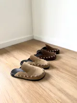 Zuecos color beige con tachas plateadas, base negra y plantilla con el logo de la marca.