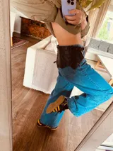 Cinturón ancho de cuero marrón oscuro con borde festoneado y cordones cruzados en la parte superior.