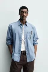 Camisa de corte regular fit confeccionada en tejido chambray de algodón con efecto lavado. Presenta cuello con botones, manga larga con puños abotonados, bolsillo en el pecho y cierre frontal de botones.
