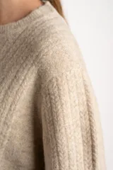 Sweater de punto color beige melange, con cuello redondo y manga larga. Presenta un tejido texturado con relieve vertical.