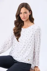 Blusa de manga larga con cuello redondo, confeccionada en tela fluida con estampado de pequeñas hojas en tono azul sobre fondo blanco. Presenta un corte holgado y un pequeño aplique metálico decorativo en el ruedo.