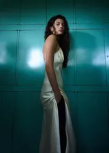 Vestido midi de tejido satinado en color beige claro, con escote halter en pico, detalles fruncidos en el pecho, tirantes finos y abertura lateral.