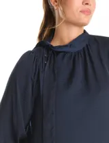 Blusa satinada de cuello alto con frunces, detalle de lazo lateral y cierre de botones. Presenta mangas largas estilo balloon con puños ajustados.
