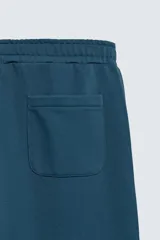 Pantalón jogger de corte relajado y pernera ancha, confeccionado en tejido de algodón con interior perchado. Presenta cintura elástica con cordón interior, bolsillos laterales y un bolsillo trasero de plastrón.