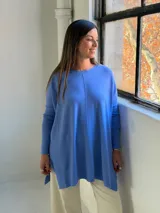 Sweater de punto color celeste, de corte holgado y diseño asimétrico con tajos laterales. Presenta cuello redondo, mangas largas y una costura vertical central en el frente.