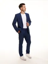 Traje de dos piezas compuesto por un saco de corte slim con solapas clásicas y bolsillos frontales, y un pantalón de corte ajustado. El conjunto presenta un diseño liso en color azul.