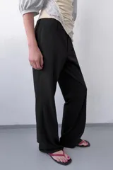 Pantalón de corte recto y tiro bajo, color marrón oscuro. Presenta trabillas en la cintura, bolsillos laterales, falsos bolsillos traseros de vivo y raya planchada en el delantero. Cierre frontal con cremallera, botón interior y ganchos metálicos.