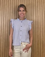 Musculosa de lino a rayas celestes y blancas, con cuello alto fruncido, cierre frontal con botones y volados en los hombros.
