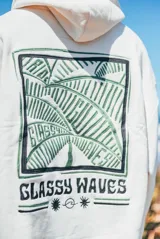 Hoodie color natural con capucha y diseño bordado en la espalda que presenta motivos de hojas de palmera y el texto 'Glassy Waves'.