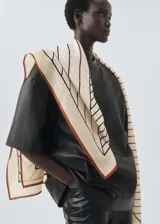 Fular cuadrado de lana con estampado geométrico en tonos beige, marrón y negro, con bordes definidos.