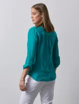 Blusa blanca de gasa marca Zac & Rachel, con cuello a la base, escote en V, abertura central con botones, bolsillo aplicado en el pecho y mangas largas regulables con presilla y botón. Tiene terminación opcional de nudo en el ruedo.