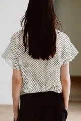 Blusa de viscosa con estampado de lunares, cuello redondo con escote en pico, volantes y lazada frontal. Presenta manga corta y bajo recto.