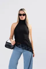Polera negra sin mangas con cuello alto, confeccionada en seda con lycra. Presenta un diseño asimétrico en el ruedo con un detalle de encaje sutil en la parte inferior.