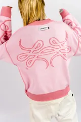 Sweater tejido reversible de corte boxy fit, con diseño gráfico de líneas curvas entrelazadas en el pecho y las mangas. Presenta un lado en tono rosa oscuro y el reverso en rosa claro, con cuello redondo y puños acanalados.