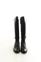 Bota de caña alta confeccionada en cuero legítimo color negro, de diseño clásico con costuras visibles y tira con hebilla lateral. Cuenta con cierre lateral interno y taco medio ancho.
