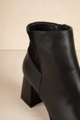 Botas de caña baja color negro, de símil cuero con punta redonda, cierre lateral, taco cuadrado y recorte en gamuza en la parte trasera.